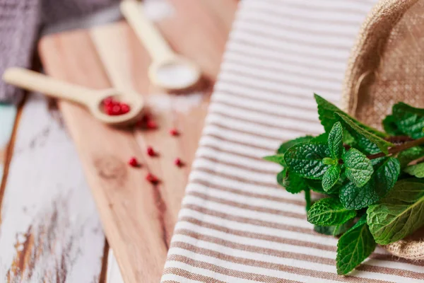 Fresh mint and wooden spoons with salt and pepper on wooden back — Stock Photo, Image