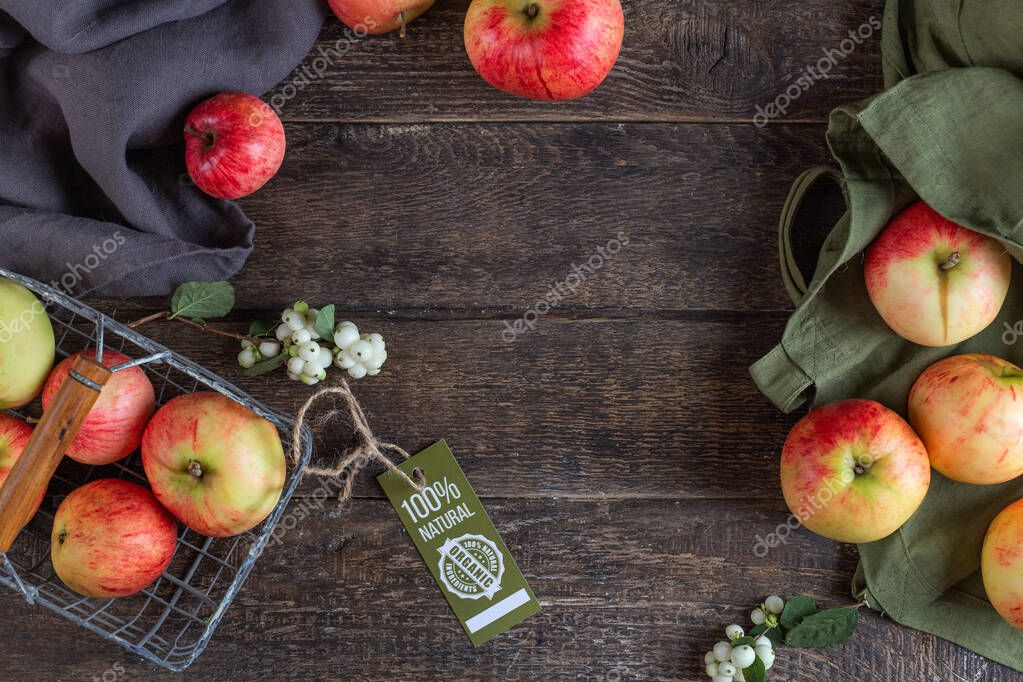 Juicy red apples and a green bag of cotton fabric with a label 100 natural product, lie on a textured table made of dark brown wood