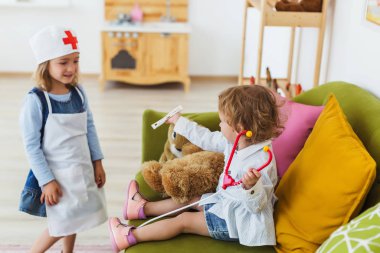 İki küçük kız rahat bir odada doktorculuk oynuyorlar..