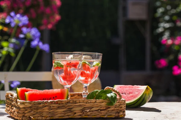 Sobre una mesa en el jardín en una canasta hay dos vasos de limonada y rebanadas de sandía — Foto de Stock