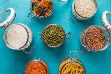 İçinde kinoa, mercimek, karabuğday, pirinç, püre, makarna olan cam kutular ve şişeler. Basit, şık bir depo. Plastik yok.