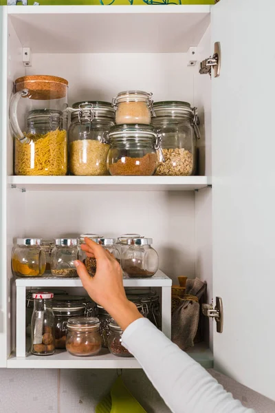 Mujer mano abre estante de la cocina con varios cereales y semillas en frascos de vidrio en los estantes de la cocina — Foto de Stock