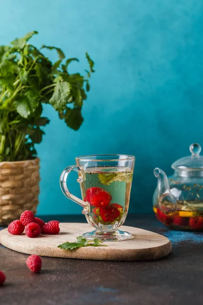 glass cup with raspberry tea mint leaves and lemon on blue