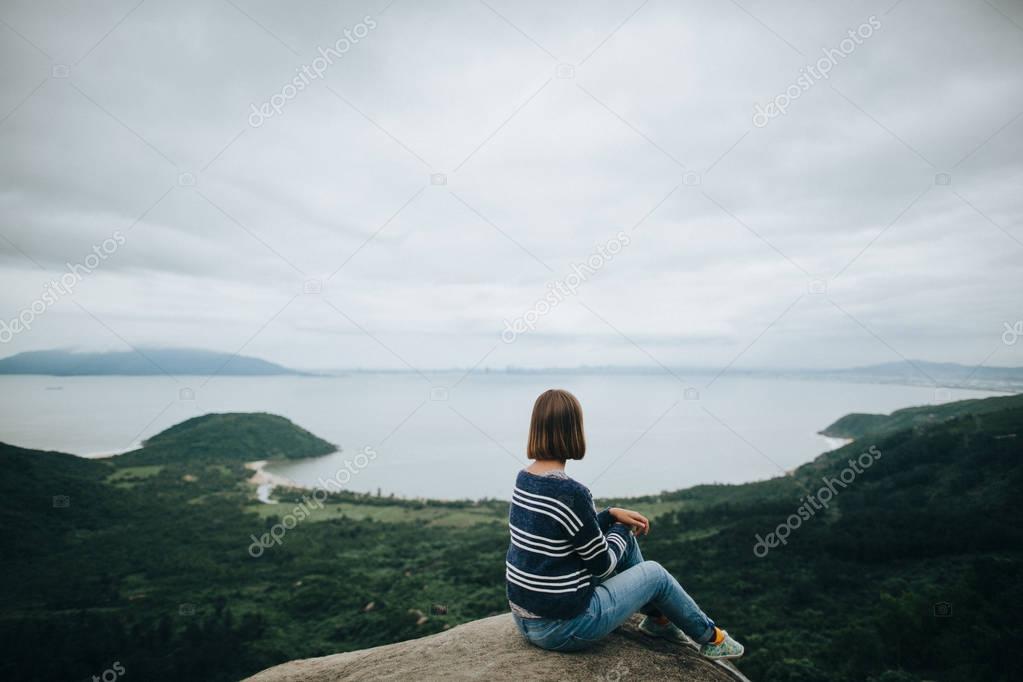 Back view of young woman sitting on cliff and enjoying amazing landscape in Hai Van Pass, Vietnam