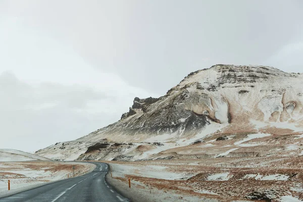 Estrada de asfalto vazia e montanhas cobertas de neve cênicas na Islândia — Fotografia de Stock
