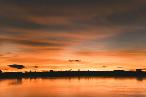 Vue panoramique de la skyline avec des arbres et des bâtiments reflétés dans l'eau au coucher du soleil, iceland — Photo de stock