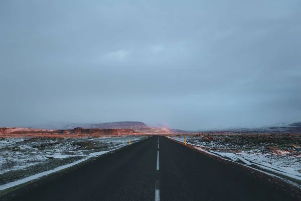 Пустая асфальтовая дорога и покрытый снегом икеландский пейзаж на рассвете — стоковое фото