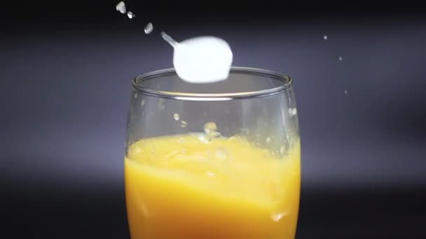 Pedaços de gelo caem em um copo com suco de laranja em um fundo preto. Movimento lento 500 FPS — Vídeo de Stock