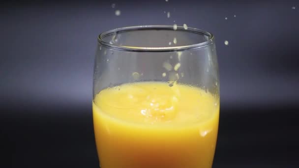 Кусочки льда падают в стакан с апельсиновым соком на черном фоне. Slow Motion 500 FPS — стоковое видео