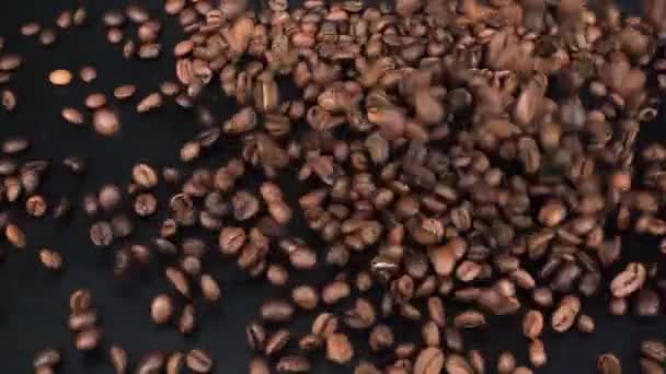 Los granos de café se derraman sobre una superficie negra . — Vídeos de Stock