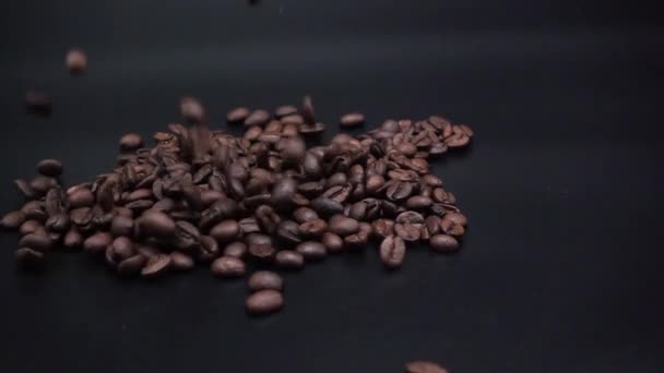 Los granos de café se derraman sobre una superficie negra . — Vídeos de Stock