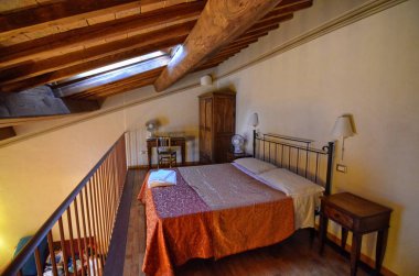 San Gimignano, Italya, Toskana bölgesi. Ağustos 14 2016. Turistler için kira için kullanılan tipik bir çiftlik evi iç. Çıplak ahşap kirişler, ferforje yatak, geniş iç mekanlara sahip tavan.