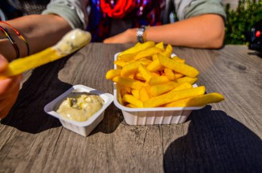 Bruges, Belçika, Ağustos 2019. Turistik Markt Meydanı 'na bakan bir kızartma dükkanı. Beyaz bir kadın tartar soslu cipslerinin tadını çıkarıyor. Patates cipsine odaklan.