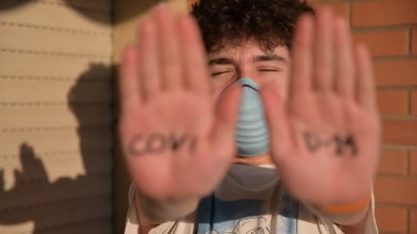 Image en gros plan des paumes des mains avec l'inscription COVID-19 d'un garçon caucasien aux cheveux bruns bouclés portant un masque bleu. Image conceptuelle du danger de contagion . — Video
