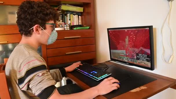 Torino, Piedmont, İtalya. Mart 2020. Koronavirüs salgını bağlamında, yaşam tarzları. Beyaz bir çocuk masaüstü bilgisayarıyla oynarken mavi koruyucu bir maske takıyor.. — Stok video