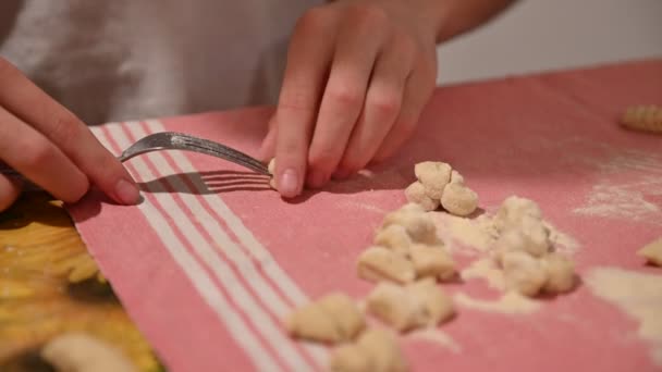 Preparación casera de albóndigas de patata. Las manos de un niño caucásico toman un pedazo de pasta y lo pasan en la parte posterior de un tenedor para darle la forma característica . — Vídeos de Stock