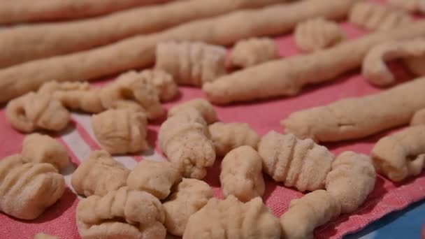 Zelfgemaakte bereiding van aardappelknoedels. Close-up image met selectieve focus op kant-en-klare gnocchi naast enkele pasta worstjes die nog verwerkt moeten worden. — Stockvideo