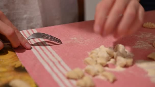 Preparación casera de albóndigas de patata. Las manos de un niño caucásico toman un pedazo de pasta y lo pasan en la parte posterior de un tenedor para darle la forma característica . — Vídeos de Stock