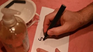 Kendini virüslerden ve bakterilerden nasıl koruyacağını. Beyaz adamın elleri dezenfektan jeliyle temizlenmiş. Arka planda koruyucu bir maske ve Covid-19 yazım durduruculu bir kağıt var..