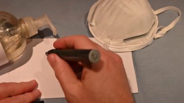 Kendini virüslerden ve bakterilerden nasıl koruyacağını. Solda bir şişe dezenfektan ve sağda bir maske. Merkezde, beyaz bir adamın el yazısının durduğu bir çarşaf var..