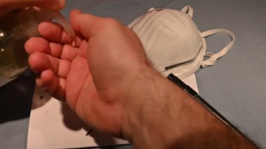 Kendini virüslerden ve bakterilerden nasıl koruyacağını. Beyaz adamın elleri dezenfektan jeliyle temizlenmiş. Arka planda koruyucu bir maske ve Covid-19 yazım durduruculu bir kağıt var..