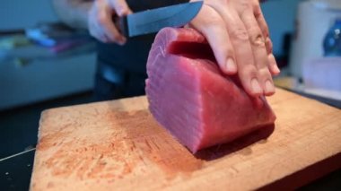 Sashimi için mavi yüzgeçli ton balığının hazırlanması: ahşap kesme tahtasının üzerinde büyük bir parça ton balığı, uzun bıçaklı beyaz bir adamın elleri güzel bir dilim kesti..