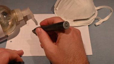 Kendini virüslerden ve bakterilerden nasıl koruyacağını. Beyaz adamın elleri dezenfektan jeliyle temizlenmiş. Arka planda koruyucu bir maske ve Covid-19 yazım durduruculu bir kağıt var..