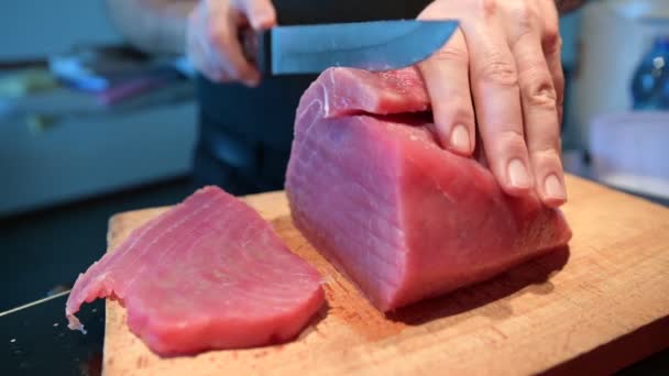 Persiapan tuna sirip biru untuk sashimi: di papan potong kayu sepotong besar tuna, sepotong telah dipotong, tangan seorang pria Kaukasia dengan pisau pisau panjang memotong sepotong bagus. — Stok Video