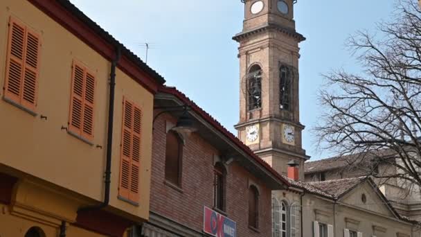 Costigliole d 'Asti, Piedmont, İtalya. Mart 2020. Kırmızı tuğlalı çan kulesindeki kamera görüntüleri. Yüksekliğiyle köy bloğunda göze çarpıyor. Beyaz arka planı ve çanları olan saati görebiliriz.. — Stok video