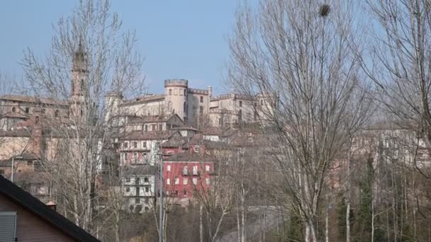 Costigliole d 'Asti, Piemont, Italia. Martie 2020. Imagini înclinate chiar în afara satului printre frunzele copacilor fără frunze iese în evidență castelul elegant cu finisaje roșii . — Videoclip de stoc