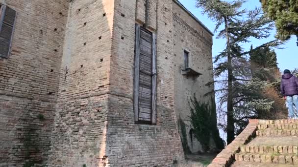 Burio, provincie Asti, Piemonte, Italië. maart 2020. Zijn kasteel is in puin: met een verlaten verschijning zijn de scheuren zichtbaar op de imposante rode bakstenen muur. Twee jongens observeren de ophaalbrug. — Stockvideo