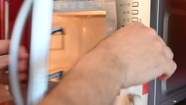 Использование микроволновой печи. Руки кавказца засунули чашку в микроволновку, затем установили таймер и запустили программу. . — стоковое видео