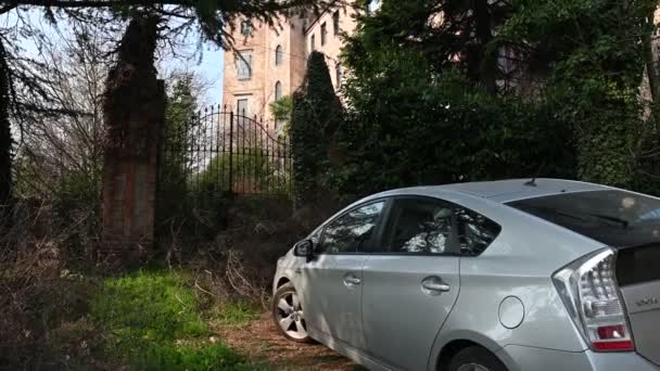 Burio, Asti ili, Piedmont, İtalya. Mart 2020. Kalenin girişine park etmiş gri metalik Toyota Prius 'un eğik görüntüsü. Bitki örtüsü onu kısmen gizliyor.. — Stok video