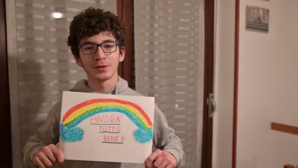 トリノ ピエモンテ イタリア 2020年3月 コルノウイルス隔離 虹の絵を手にした茶色い巻き毛と眼鏡を持つ白人の少年の肖像画とメッセージは大丈夫でしょう — ストック動画