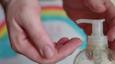Virüslerin ve bakterilerin nasıl öldürüleceğini. Şişe hortumuna seçici bir odaklanma ile yakın çekim yap. Beyaz adamın eli maske bırakır ve jel dağıtır. Eller, bulanık arka planda gökkuşağı tasarımıyla, yıka