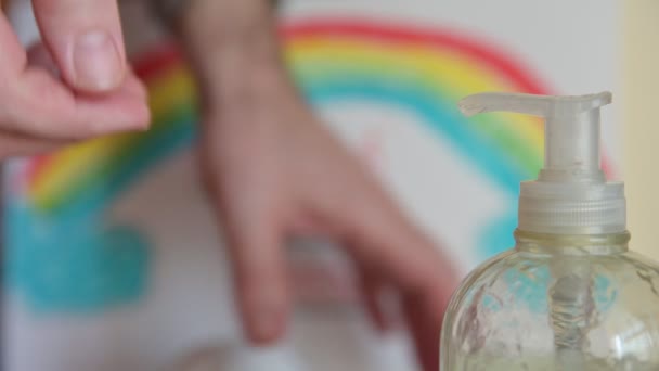 How to kill viruses and bacteria. Close up shot on bottle spout with selective focus. Caucasian man's hand leaves mask and dispenses gel. The hands, on the blurred background with rainbow design, wash — Stock Video