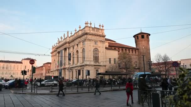 Turim, região do Piemonte. Itália, fevereiro de 2020. Filmagem com movimento pan na Piazza Castello em direção ao palácio real. O sol da tarde ilumina a fachada. Pessoas passeiam, passando carros — Vídeo de Stock