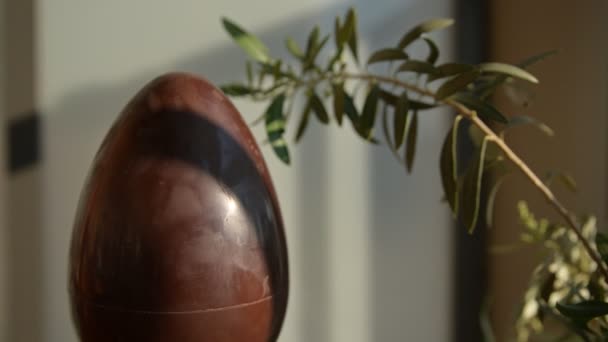 Imagen conceptual de primer plano de la Pascua en el momento de la pandemia del coronavirus. Un huevo de chocolate con una rama de olivo al lado. Caucásico hombre manos poner una máscara protectora azul en el huevo . — Vídeo de stock