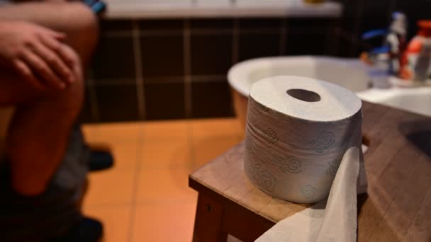 Close up shot of toilet paper.In the background the legs of a Caucasian man while defecating.Hands drum with fingers. The right hand tries to grab the toilet paper, fails. — Stock Video