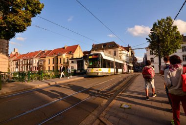 Gent, Belçika, Ağustos 2019. Şehre hizmet eden tramvaylar sessizce ve verimli bir şekilde çalışır. Şehir kanallarından birinin üzerinden bir tramvay geçiyor, öğleden sonra ışığı altında, insanlar kaldırımda..