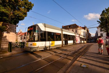 Gent, Belçika, Ağustos 2019. Şehre hizmet eden tramvaylar sessizce ve verimli bir şekilde çalışır. Şehir kanallarından birinin üzerinden bir tramvay geçiyor, öğleden sonra ışığı altında, insanlar kaldırımda..