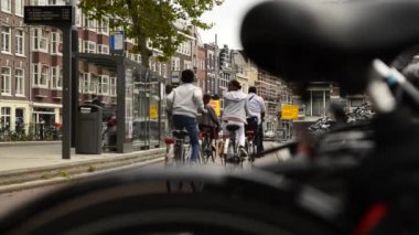 Amsterdam, Hollanda - Ağustos 2019: Bulanık bir çerçeveden ve park halindeki bir bisikletin eyerinden bisikletçilerin bisiklet yolundan geçtiğini görüyoruz. Biraz daha sola, tramvay durağına.. 