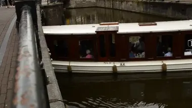 Amsterdam, Hollanda - Ağustos 2019: Tarihi merkezde, genelev bölgesindeki kanallardan biri. Bir turist teknesi bir kanaldan diğerine taşınıyor..