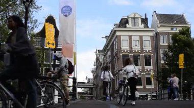 Amsterdam, Hollanda - Ağustos 2019: Bisiklet yolunun aşağısından bakış açısı: motorlar kanal üzerindeki köprüden gelir ve döner. Arka planda tarihi merkezin karakteristik evleri var..