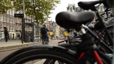Amsterdam, Hollanda - Ağustos 2019: Bulanık bir çerçeveden ve park halindeki bir bisikletin eyerinden bisikletçilerin bisiklet yolundan geçtiğini görüyoruz. Biraz daha sola, tramvay durağına..