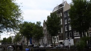 Amsterdam, Hollanda - Ağustos 2019: Tarihi merkezde, genelev bölgesinde kanal tiplerine eğilim. Evler kanalın suyuna yansıyor, insanlar arka plandaki köprüden geçiyor..