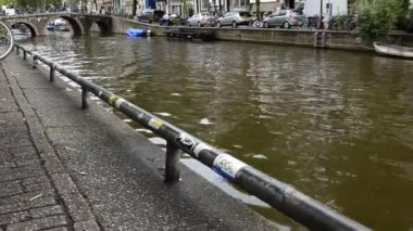 Amsterdam, Hollanda - Ağustos 2019: Tarihi merkezde, genelev bölgesinde kanal tiplerine eğilim. Evler kanalın suyuna yansıyor, insanlar arka plandaki köprüden geçiyor..