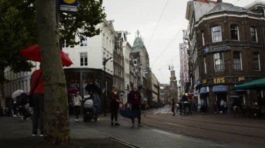 Amsterdam, Hollanda - Ağustos 2019: Tarihi merkezde yağmur durdu ve yoldan geçenler şemsiyeyi kapattı. Arka planda şehrin simgelerinden biri olan nane kulesini görebilirsiniz..