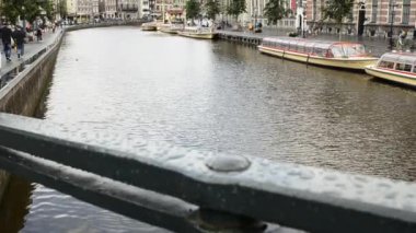 Amsterdam, Hollanda - Ağustos 2019: Tipik evlerle çevrili eski şehrin büyüleyici kanalları. İnsanlar kanalda, demirlemiş turist tekneleriyle yürüyor. Kara bulutlu gri bir gün. Eğim hareketi.