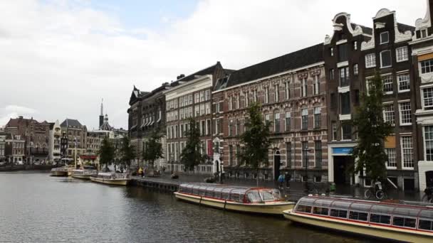 アムステルダム オランダ 2019 典型的な家に囲まれた旧市街の魅力的な運河 人々は運河 係留観光船に沿って歩く 暗い雲と灰色の日 パン運動 — ストック動画